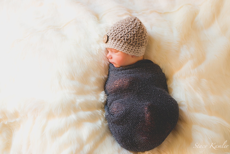 Newborn baby boy in a blue stretch wrap and a brown hat